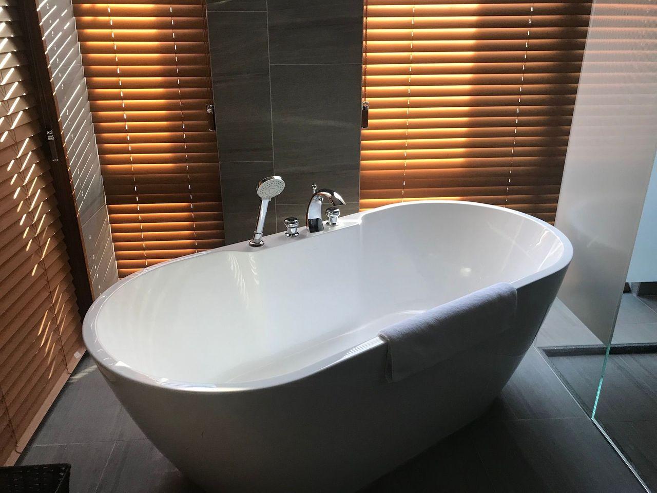 Luxurious oval bathtub with a towel, surrounded by ambient blinds at Dongdaemun Novotel Ambassador Hotel.